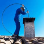 spazzacamino vestito di blu con scovolo pulisce una canna fumaria dal tetto